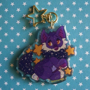 May include: Purple and white furry cartoon wolf with a galaxy print on its neck and tail. The wolf is holding a blue and white ball. The wolf is surrounded by yellow stars. The image is a keychain.