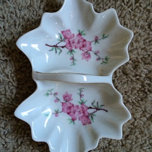 May include: A white porcelain divided dish with a floral design. The dish has a scalloped edge and a handle in the center. The flowers are pink and green.