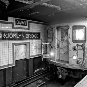 May include: Black and white photo of a subway train arriving at a station. The station platform has white tile walls with the words "City Hall" and "BROOKLYN BRIDGE" in black lettering.