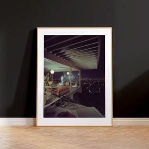 May include: A framed photograph of a modern home with a view of a city skyline at night. The home has a large window and a balcony with furniture. The city lights are visible in the distance.
