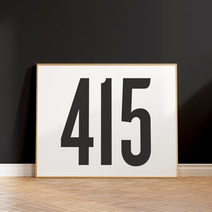 Op de afbeelding: Een ingelijst print met het nummer 415 in vetgedrukte zwarte letters op een witte achtergrond. De lijst is van licht hout.