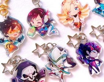 Op de afbeelding: Een set van tien Overwatch-personage sleutelhangers. De sleutelhangers zijn gemaakt van helder acryl en hebben chibi-stijl illustraties van personages uit de game. De personages zijn Tracer, Mercy, Reaper, D.Va, Genji, Sombra, Widowmaker en Reinhardt. Elke sleutelhanger is bevestigd aan een zilveren stervormige hanger.