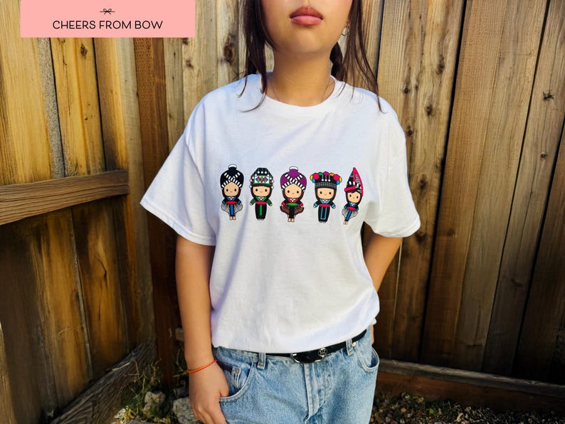 May include: White t-shirt featuring a row of six cartoon figures in traditional outfits. Each figure has a unique hat and outfit design. The text "CHEERS FROM BOW" is in a pink rectangle at the top.