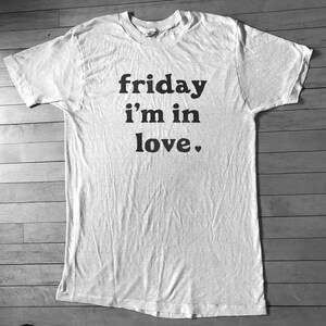 May include: White t-shirt with black text that reads "friday i'm in love."