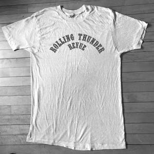 May include: A white t-shirt with the text "Rolling Thunder Revue" printed in black on the front.