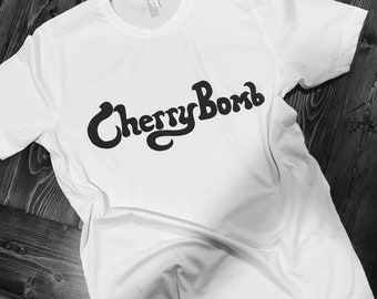 May include: White t-shirt with a black graphic that says "Cherry Bomb" in a retro font.