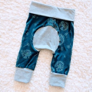 May include: Teal baby pants with a dandelion print and gray cuffs. The pants have a gray patch on the back.