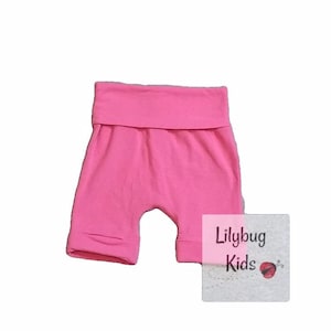 May include: Pink cotton baby shorts with a wide elastic waistband. The shorts are made by Lilybug Kids.