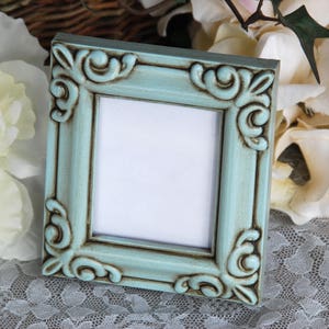 May include: A light blue picture frame with ornate detailing and a distressed finish. The frame has a white mount and is ready to display a photo or artwork.
