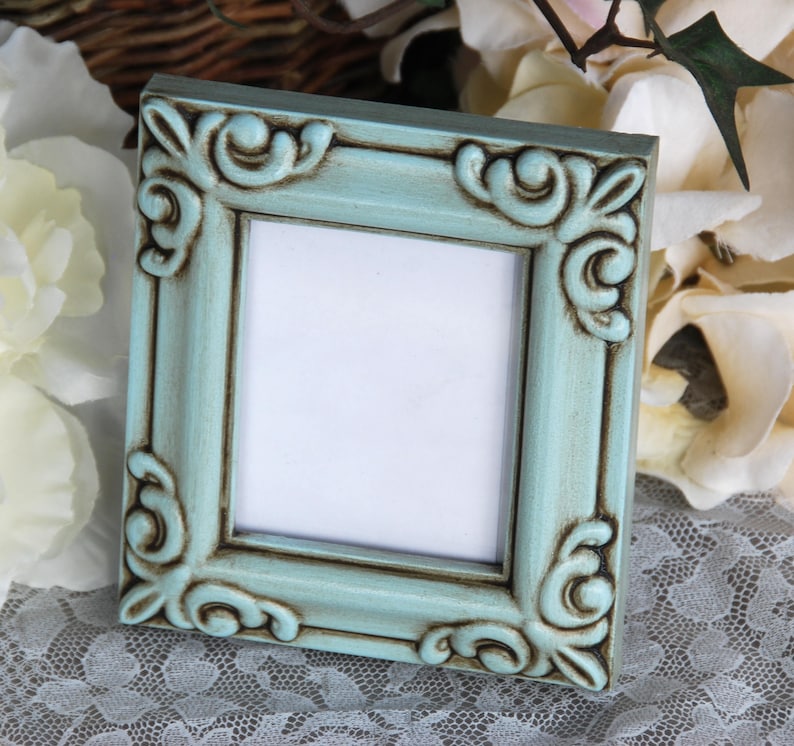 May include: A light blue picture frame with ornate detailing and a distressed finish. The frame has a white mount and is ready to display a photo or artwork.