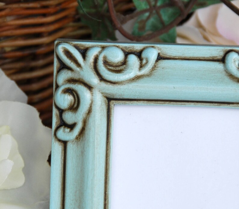 May include: A light blue picture frame with ornate detailing and a distressed finish. The frame has a white mount and is ready to display a photo or artwork.