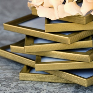 May include: A stack of six gold picture frames with a textured finish. The frames are stacked on top of each other, with the largest frame on the bottom and the smallest frame on top.