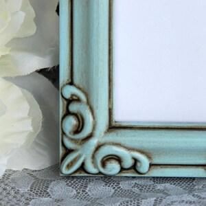 May include: A teal picture frame with ornate detailing and a distressed finish. The frame is made of wood and has a light blue paint colour.
