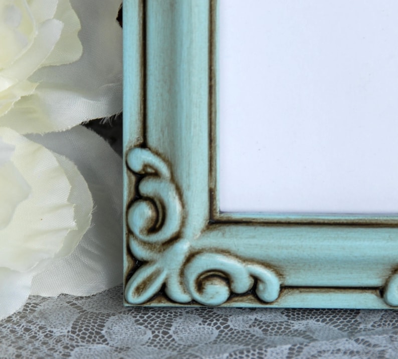 May include: A teal picture frame with ornate detailing and a distressed finish. The frame is made of wood and has a light blue paint colour.
