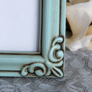 May include: A light blue picture frame with a distressed finish and ornate detailing. The frame has a white mount and is made of wood.