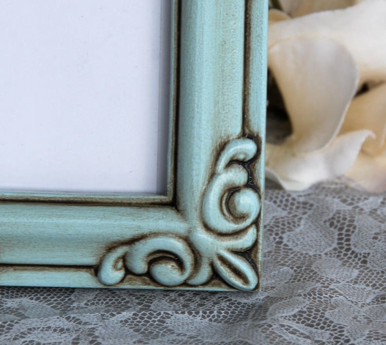 May include: A light blue picture frame with a distressed finish and ornate detailing. The frame has a white mount and is made of wood.