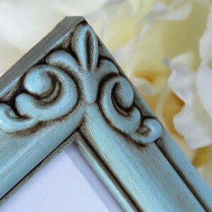 May include: A close-up of a teal blue picture frame with ornate detailing. The frame has a distressed finish with brown accents.