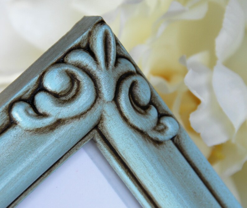May include: A close-up of a teal blue picture frame with ornate detailing. The frame has a distressed finish with brown accents.
