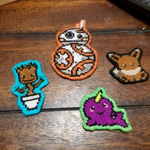 May include: Four embroidered patches featuring popular characters. A brown and white BB-8, a brown and white Groot, a brown Eevee, and a purple unicorn.