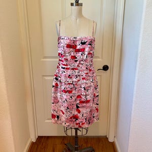 May include: A pink floral print dress with spaghetti straps displayed on a mannequin. The dress features a pattern of pink, red, and black flowers. The dress is knee-length and has a layered design.