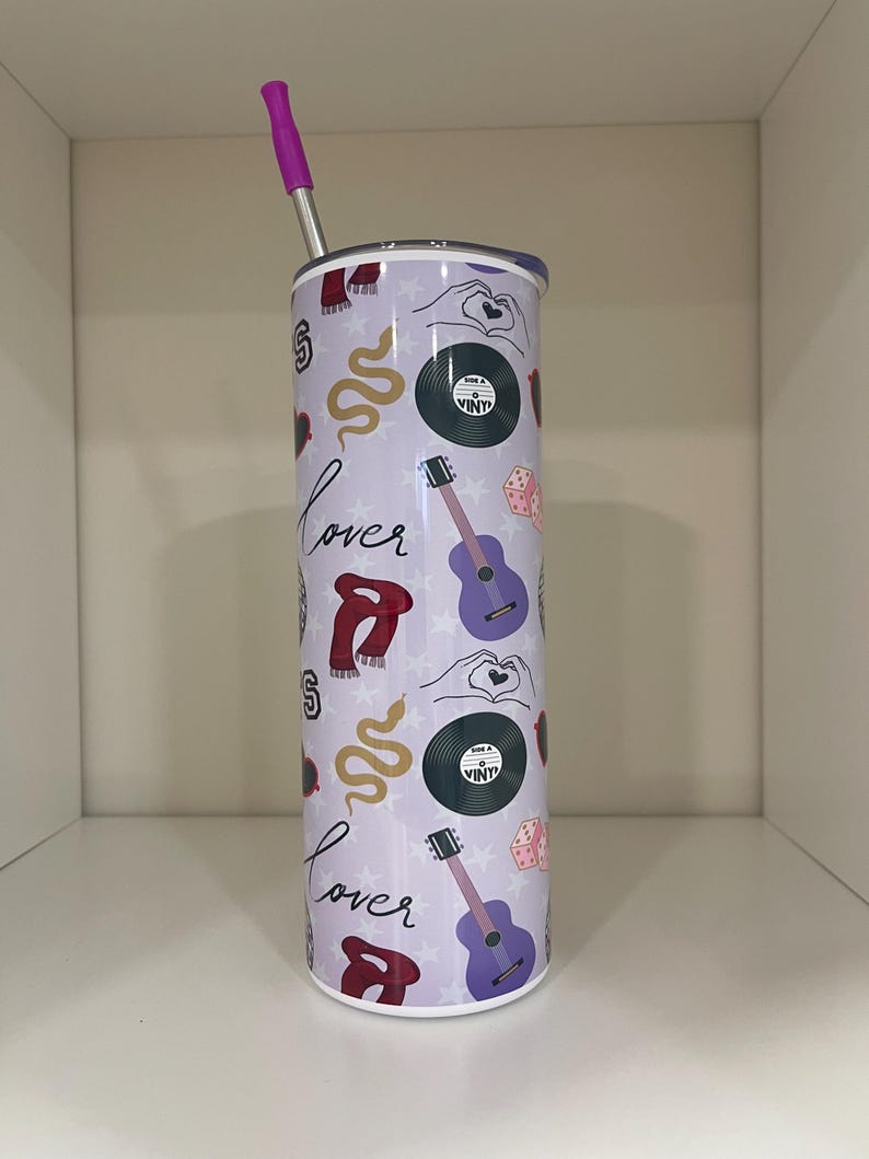 May include: A stainless steel tumbler with a purple lid and straw. The tumbler is covered in a pattern of musical and romantic symbols, including guitars, vinyl records, and the word "Lover". The background is a light purple color.