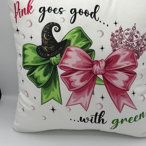 Peut inclure: Coussin décoratif blanc avec le texte "Pink goes good...with green." Il présente un nœud vert, un nœud rose, un chapeau de sorcière et une couronne rose. Des bulles et des étoiles parsèment le motif.