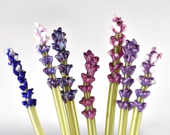 May include: A bouquet of seven glass lavender flower stems in shades of purple, blue, and white. The stems are a light green color.