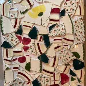 May include: A mosaic art piece made from broken pieces of ceramic plates. The pieces are arranged in a pattern of red, green, and white flowers on a white background.