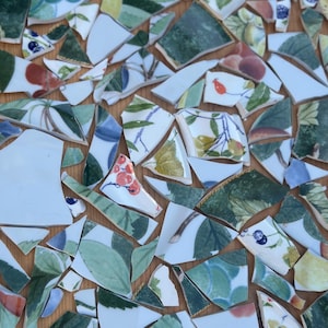 May include: Close-up of a mosaic tabletop made from broken ceramic pieces. The fragments feature floral and fruit designs in green, red, blue, and white, arranged on a wooden surface. The mosaic art showcases a unique, handcrafted aesthetic.