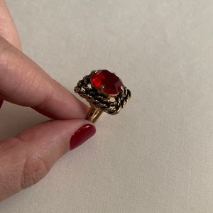 May include: A gold ring with a red gemstone set in a rope-like design.