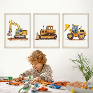 May include: Three framed watercolour illustrations of yellow construction vehicles. The illustrations are of a backhoe, a bulldozer, and a dump truck. The illustrations are on a white background.