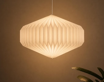 Peut inclure: Une suspension lumineuse blanche, plissée, de style lanterne avec une forme géométrique hexagonale. La lampe est suspendue par un cordon vertical fin et émet une lueur chaude et douce, créant un effet de lumière diffuse sur sa surface texturée.