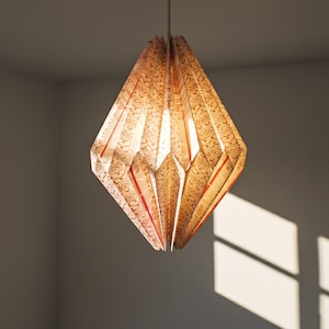 Puede incluir: Una lámpara colgante en forma de diamante. La pantalla está hecha de papel plegado con un patrón repetitivo en beige y rojo. La luz cuelga de un cable fino.