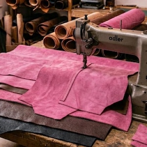 May include: A workshop with an Adler sewing machine and pink and brown leather sheets on a wooden table. Shelves in the background display rolls of leather and tools. The text "Leather Sheets" is visible at the bottom of the image.