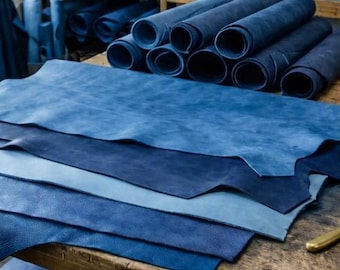 May include: Multiple sheets of blue leather are stacked on a wooden workbench. Several rolls of blue leather are arranged in a pile on the table, while additional rolls are stored on wooden shelves in the background of the workshop.