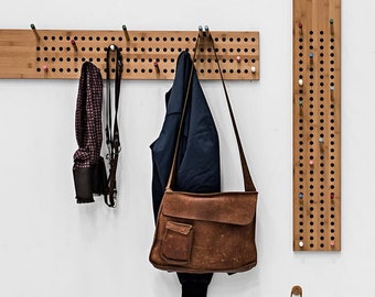 May include: Wooden wall-mounted storage system with coat racks, shelves, and pegboards. Includes a brown leather satchel, a navy blue jacket, and various shoes. The shelves are made of wood and are approximately 36 inches long.