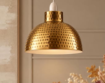 May include: A dome-shaped pendant light fitting with a metallic gold finish and a hammered, dimpled texture. The lamp features a white cord and a white cylindrical top mount, casting a warm glow from the open bottom of the shade.