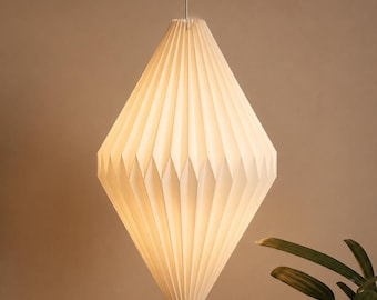 May include: A white, diamond-shaped pendant lamp with a pleated paper texture. The light fitting hangs from a thin cord, emitting a soft, warm glow through its folded structure, creating a symmetrical, geometric silhouette.