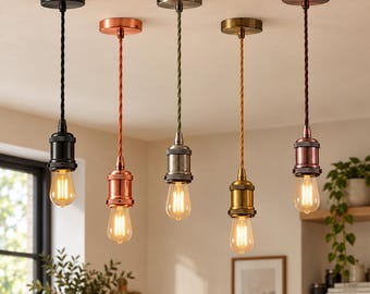 May include: Five pendant lights hanging from a ceiling, each featuring a different metallic finish including black, copper, silver, brass, and bronze. Each light has a twisted fabric cord and a clear glass Edison-style light bulb.