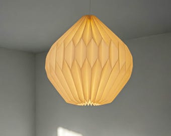 May include: A cream-coloured pendant light with a geometric, pleated, diamond-patterned shade. The lamp is suspended from a thin cord and emits a warm, soft glow, highlighting the intricate folded structure of the material throughout the surface.