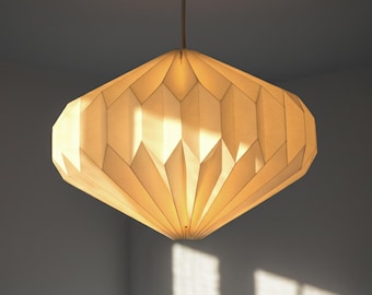 May include: A cream-colored pendant light with a geometric, pleated paper shade. The lantern features a diamond-like, faceted structure that emits a warm, diffused glow from within, suspended by a thin cord from the ceiling above.