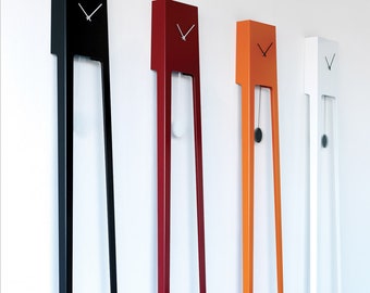 May include: Four contemporary wall clocks in black, red, orange, and white. Each clock features a rectangular head with a clock face and long, thin legs. The orange clock has a black pendulum. The clocks are mounted on a white wall.