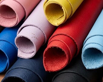 May include: A collection of rolled leather sheets in various colours including pink, light purple, yellow, red, light blue, dark blue, and black. Each roll displays a textured surface and a visible raw edge, showcasing the material's thickness.