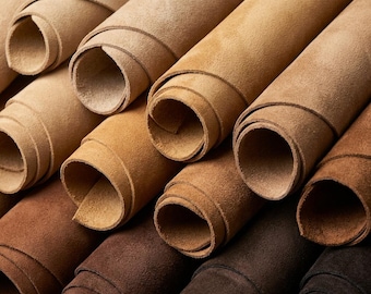 May include: A collection of multiple rolls of suede leather arranged in a stacked formation. The rolls display a gradient of earth tones, ranging from light beige and tan to medium brown, dark chocolate, and deep espresso shades.