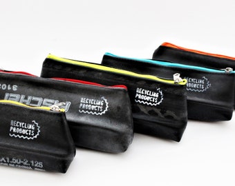 May include: Five black zippered pouches made from recycled bicycle inner tubes. Each pouch has a different colored zipper pull and the text "RECYCLING PRODUCTS" printed on the front.
