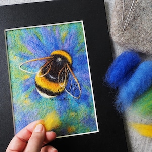 May include: A needle felted bumble bee on a blue flower. The bee is yellow and black with a fuzzy texture. The flower is blue and purple with a green center. The image is signed "The Lady Moth".