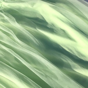 May include: Pale green tulle fabric with a soft, flowing texture. The fabric is sheer and delicate, with a subtle sheen.