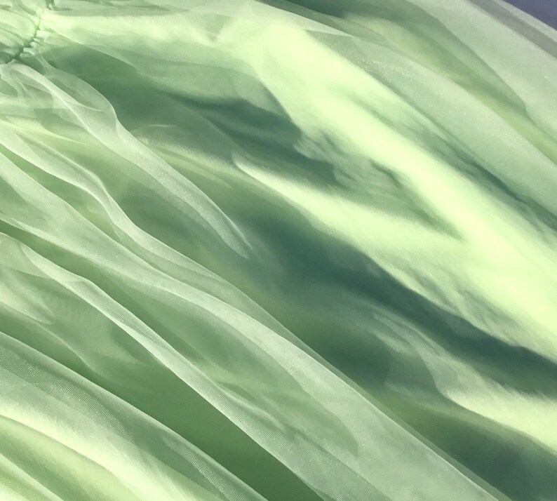 May include: Pale green tulle fabric with a soft, flowing texture. The fabric is sheer and delicate, with a subtle sheen.