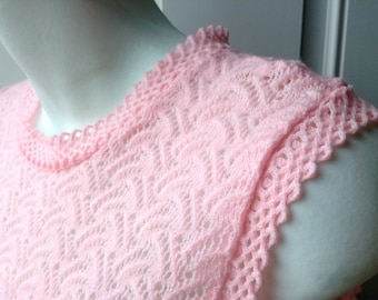 May include: A pink crocheted top with a delicate lace pattern. The top has a round neckline and a scalloped edge.
