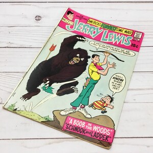 May include: A vintage comic book cover featuring Jerry Lewis in a yellow shirt and red bow tie. The cover features a cartoon illustration of Jerry Lewis with a bear and a young boy. The comic book is titled "Jerry Lewis" and the tagline is "America's Funniest Comic Mag!" The cover also includes the text "I shot an arrow into the air. It fell to earth, I know not where."